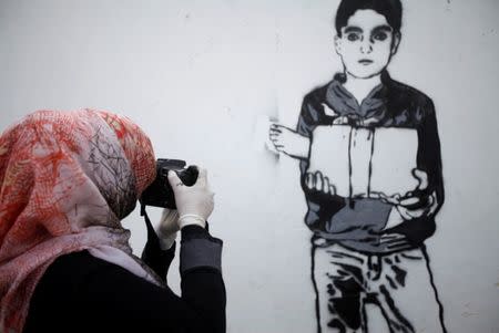 An artist takes pictures of a mural she painted as part of the "Silent Victims" campaign to depict the suffering of women and children in the war-torn Yemen, in Sanaa, Yemen March 1, 2018. REUTERS/Mohamed al-Sayaghi