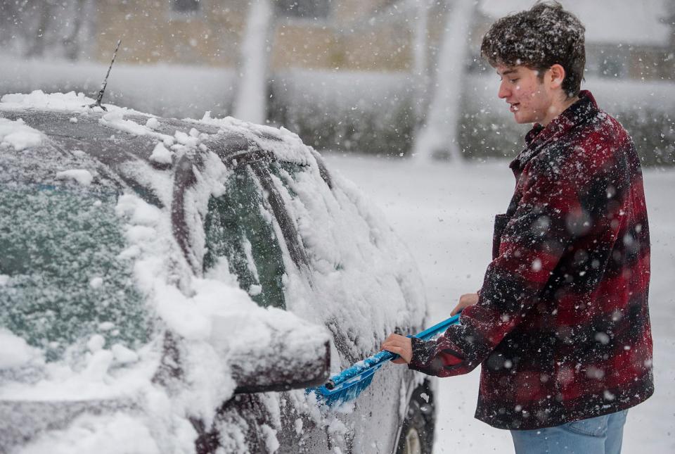 Zach Troderman, a senior at Framingham High School, brushes snow off his car after school earlier today, Jan. 23, 2023.