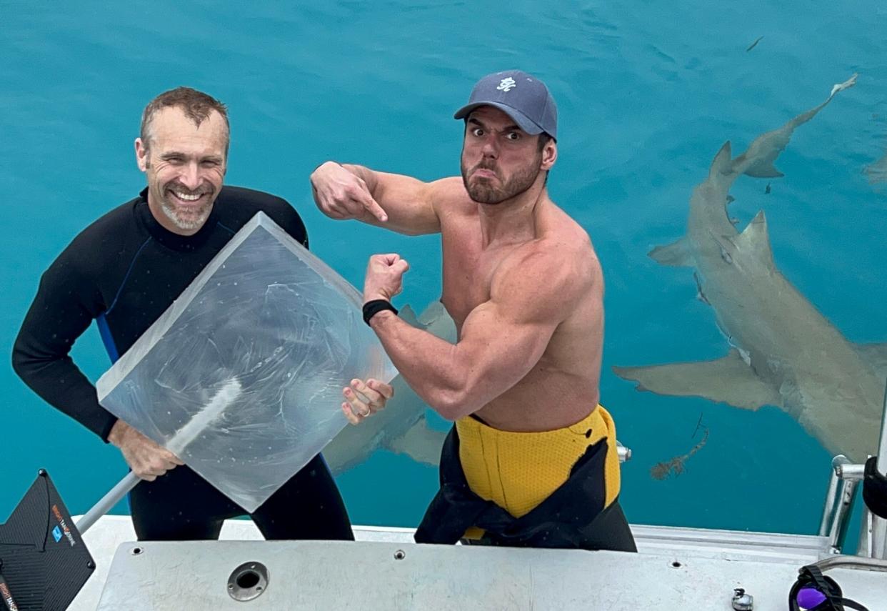 Mike Heithaus and Ross Edgley on a boat with sharks swimming behind and Heithaus holding a giant piece of gelatin