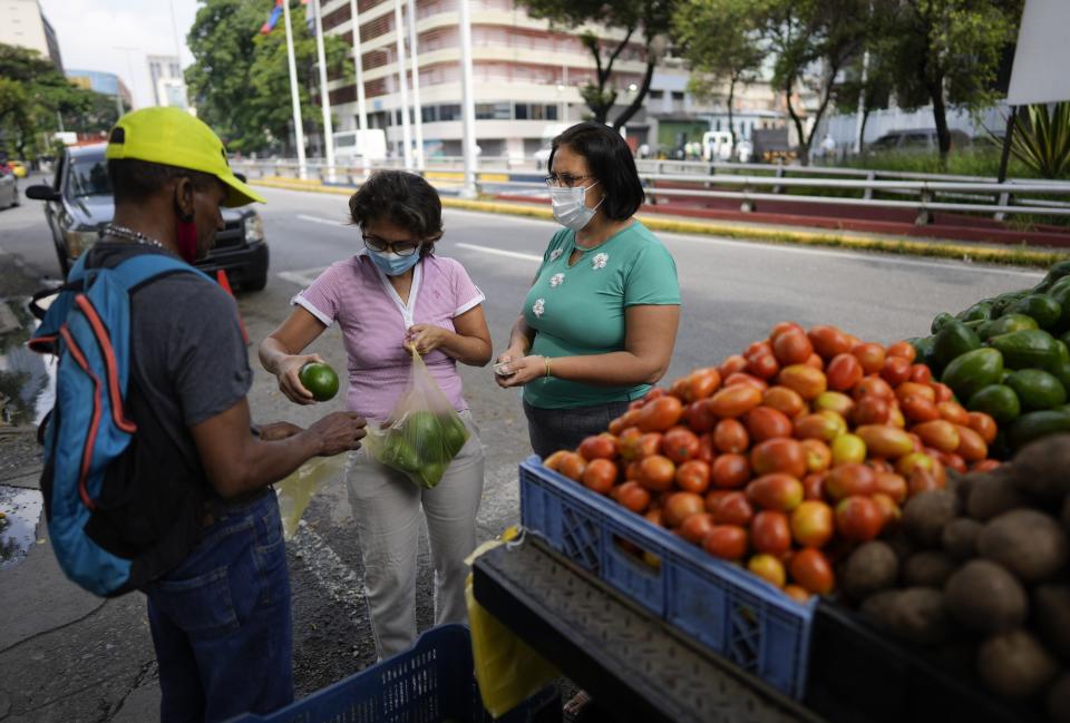 A woman purchases avocados from a produce vendor in Caracas, Venezuela, Friday, Oct 1, 2021. A new currency with six fewer zeros debuts today in Venezuela, whose currency has been made nearly worthless by years of the world's worst inflation. The new currency tops out at 100 bolivars, a little less than $25 until inflation starts to eat away at that as well. (AP Photo/Ariana Cubillos)