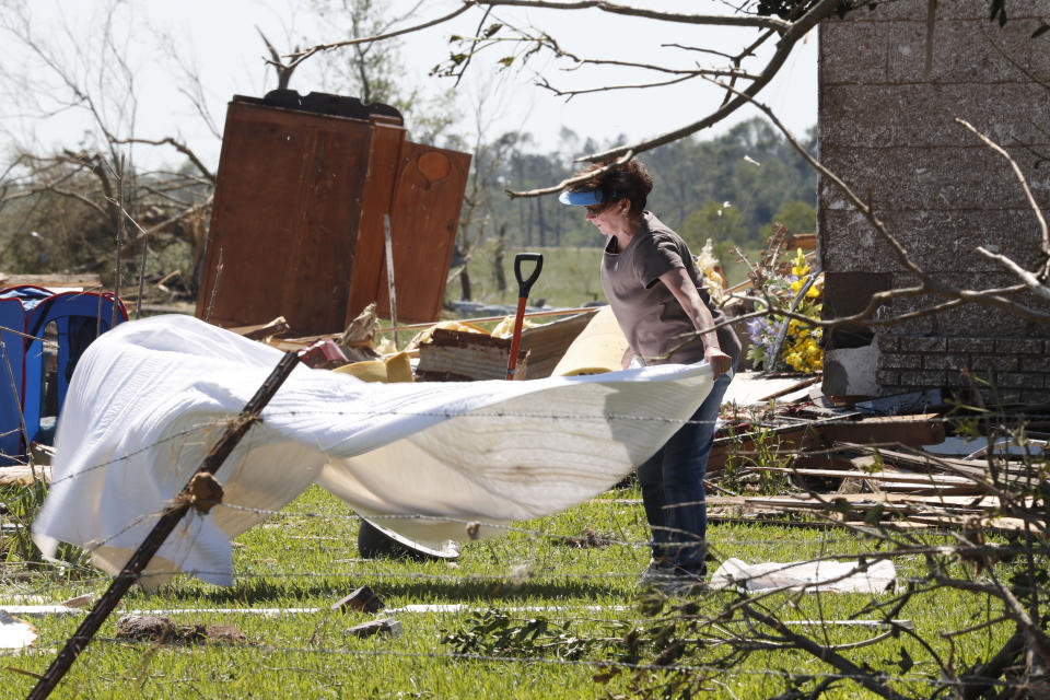 Diana Gray, stretches out a wet cover to dry outside her cousin's tornado damaged house in the Williamsburg community in rural Jefferson Davis County, Miss., Tuesday, April 14, 2020. The house was one of at least 100 heavily damaged or destroyed by Sunday's tornado that swept through the county as part of a system that spawned several other tornadoes that caused widespread damage and killed at least 12 people. (AP Photo/Rogelio V. Solis)