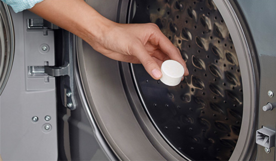 a hand placing an affresh cleaning tablet into a washing machine