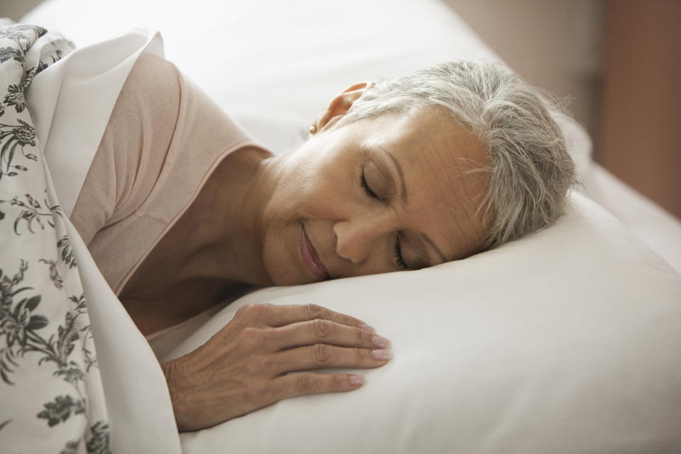 Adult woman with grey hair sleeping in bed.