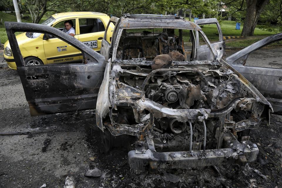 A taxi drives past the charred remains of a car that was burned during clashes between Indigenous people from Cauca state who arrived to support the national strike, with local residents who do not support the blocking of roads in Cali, Colombia, Monday, May 10, 2021. Colombians have protested across the country against a government they feel has long ignored their needs, allowed corruption to run rampant and is so out of touch that it proposed tax increases during the coronavirus pandemic. (AP Photo/Andres Gonzalez)