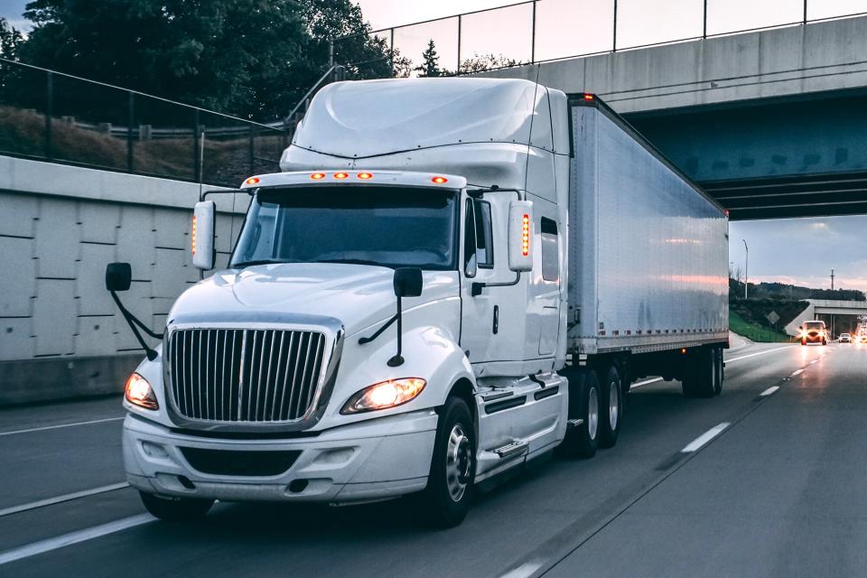 White 18 wheeler tractor trailer semi-truck on the highway at dusk