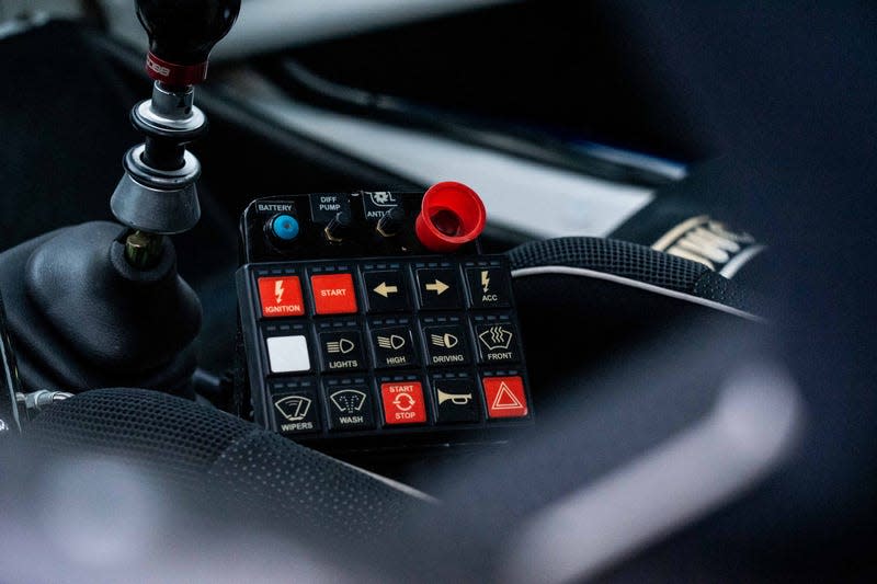 close-up interior photo of a racing-style control panel in the center console of a subaru 2.5rs built for rally racing. buttons for ignition, engine start, turn signals, headlights, wipers and defroster can be seen