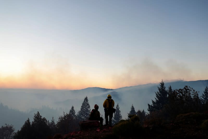 Two firefighters watch from the top of a hill as the Kincade fire burns below in Calistoga, California