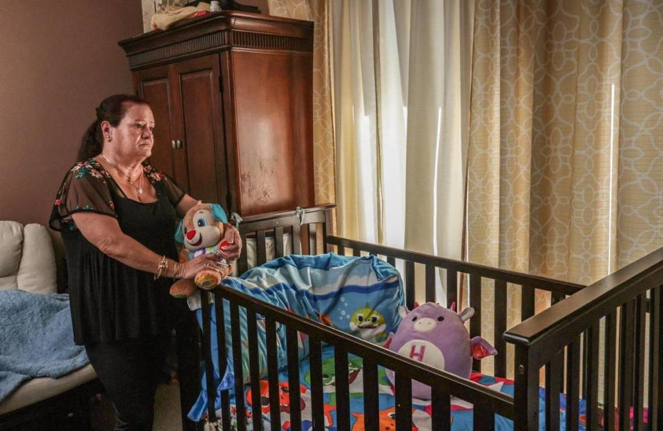 Holding a stuffed toy, Amparo Gonzalez knows her grandson, Royce Aguerro, 3, has outgrown the crib she leans on but does not have the funds to purchase a bed for his bedroom. Gonzalez, shown here on November 23, 2021 in her home in Homestead, cares for her two grandchildren, Royce and his 18-year-old sister Annalis. Her youngest daughter and the mother of her grandchildren died two years ago.