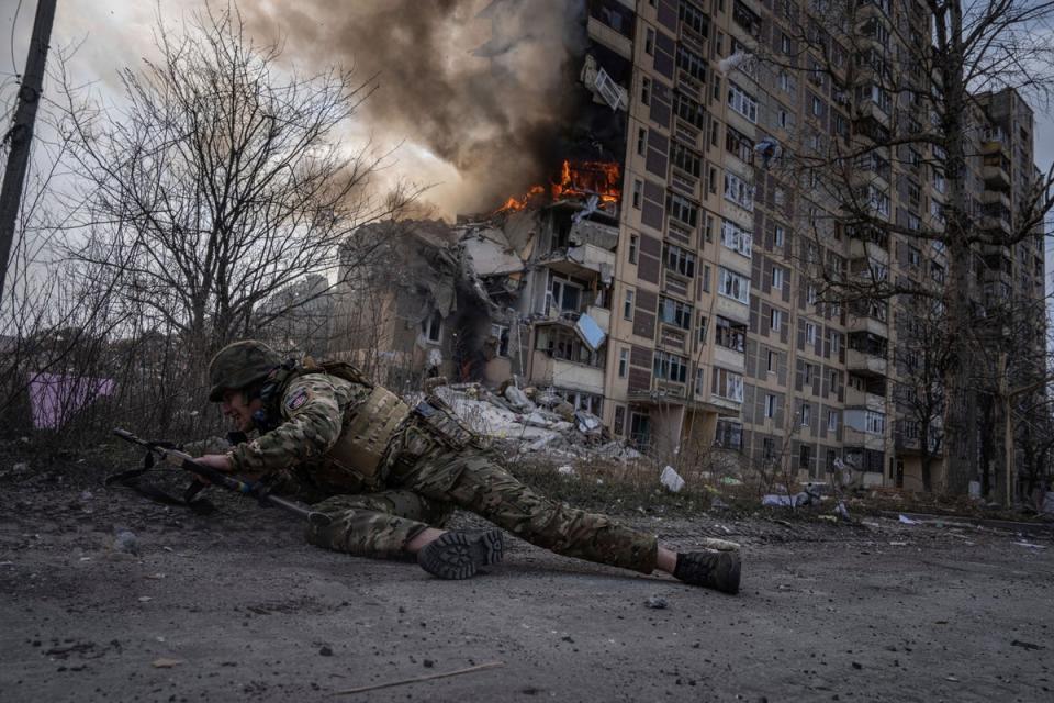 A Ukrainian police officer takes cover in front of a burning building that was hit in a Russian airstrike in Avdiivka (AP)