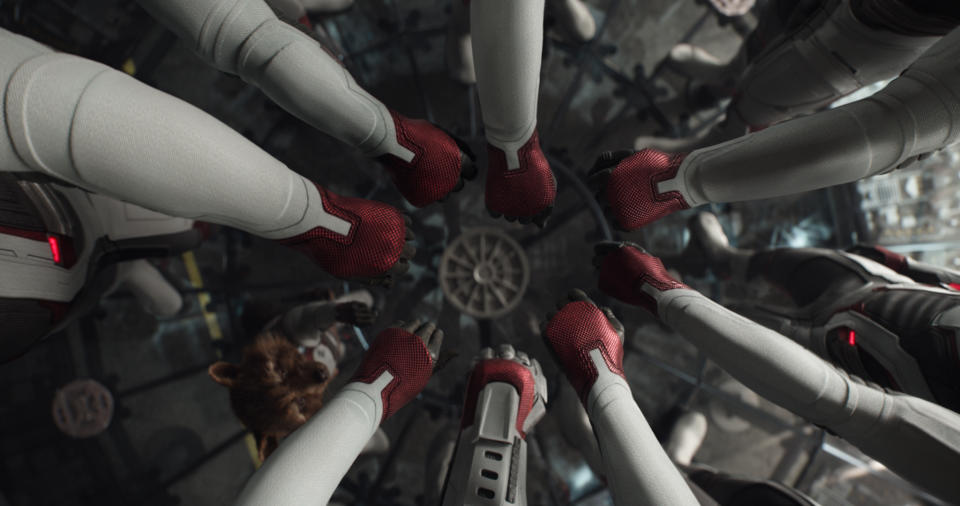 The Avengers put their hands in a circle, while Rocket Raccoon reaches up to join them, in a scene from Avengers: Endgame.