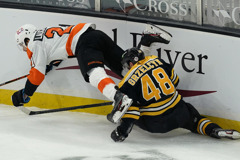 Philadelphia Flyers left wing Scott Laughton (21) and Boston Bruins defenseman Matt Grzelcyk (48) grapple for the puck along the boards during the second period of an NHL hockey game Thursday, Jan. 21, 2021, in Boston. (AP Photo/Elise Amendola)