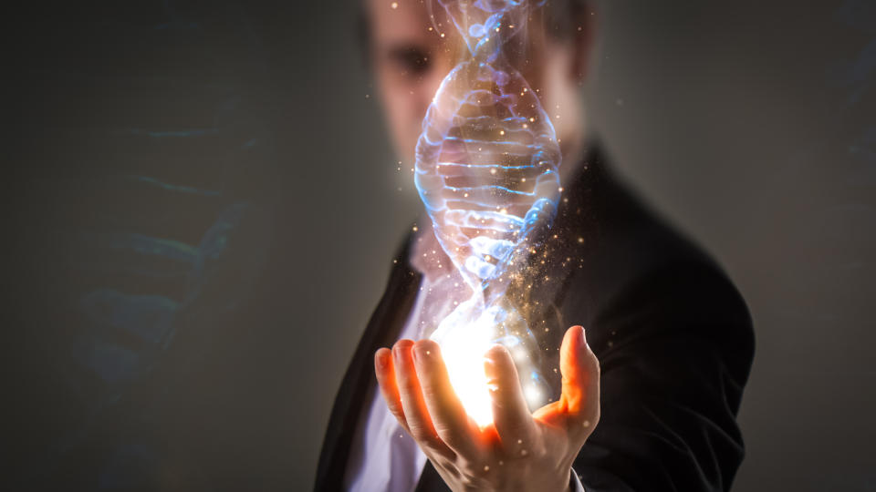 Man in a suit with a 3D holographic image of a DNA strand being projected from his open, outstretched hand.