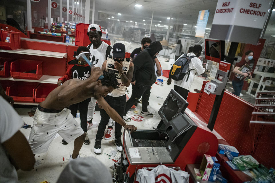 In this Wednesday, May 27, 2020 photo, a looter uses a claw hammer as he tries to break in to a cash register at a Target store in Minneapolis. Rioters ignited fires and looted stores all over the city, as peaceful protests turned increasingly violent in the aftermath of the death of George Floyd. (Richard Tsong-Taatarii/Star Tribune via AP)