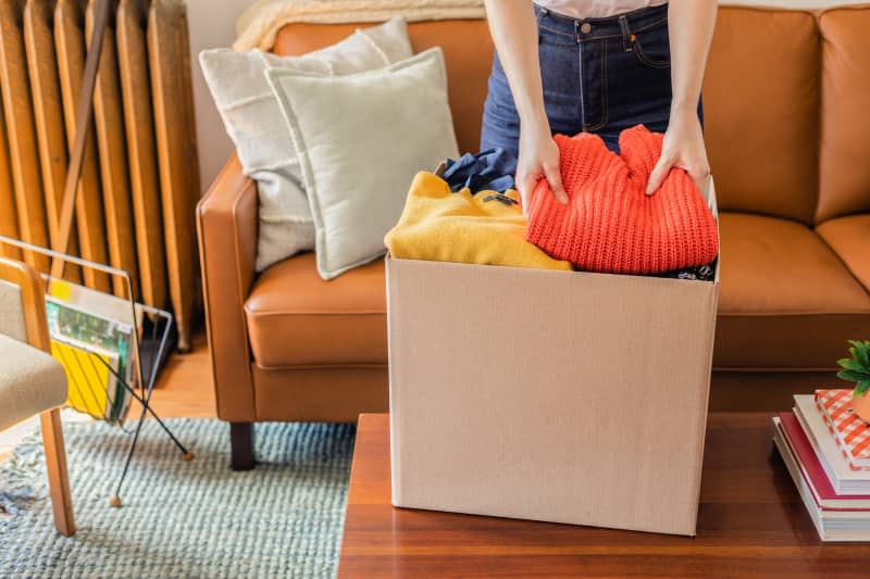 cardboard box with someone putting clothes in on coffee table