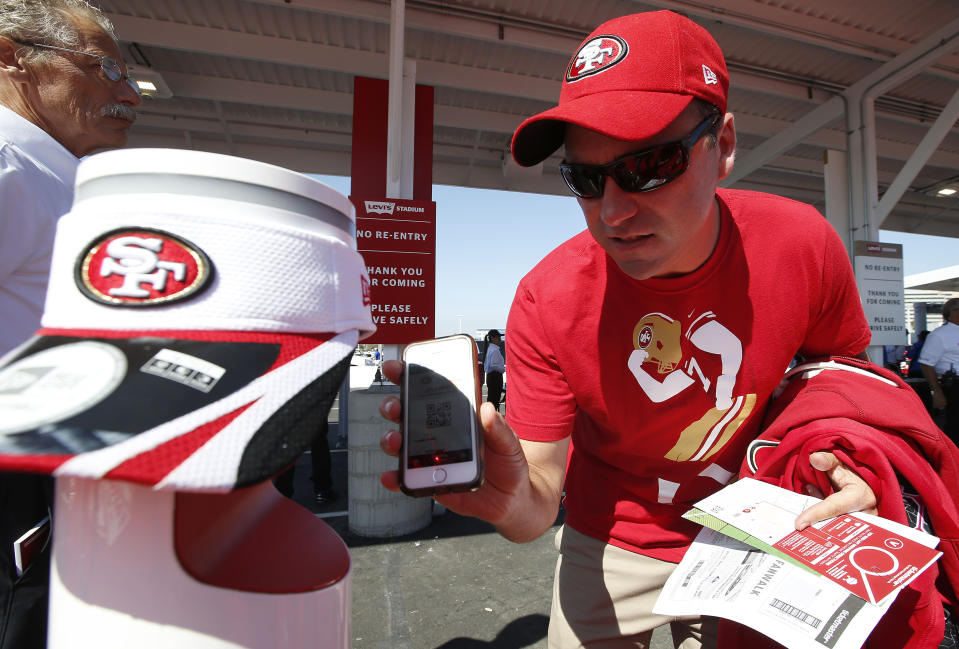 FILE - In this Aug. 17 2014, file photo, a fan uses a smart phones to scan tickets at Levi's Stadium before an NFL preseason football game between the San Francisco 49ers and the Denver Broncos in Santa Clara, Calif. Tickets have widely transitioned from paper souvenirs to smartphone screens. These tools are an important piece of the reopening puzzle. They also further test a fan’s willingness to potentially sacrifice a little more privacy in an increasingly wired-in world in exchange for the opportunity to sit courtside or behind the plate again. (AP Photo/Tony Avelar, File)