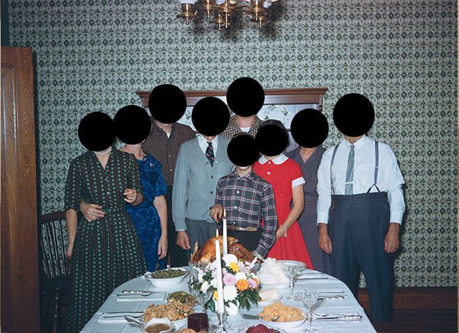 Group of people standing around a dining table with a meal prepared, heads obscured by black circles for privacy