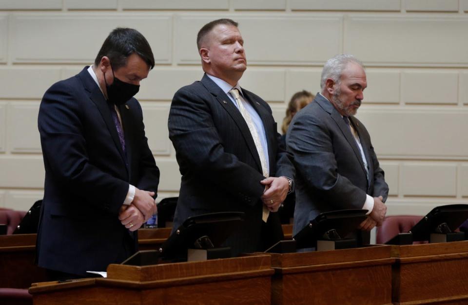 From left, Republican Representatives Brian Newberry, David Place and Justin Price stand for the opening invocation and pledge in the House on Tuesday. Place and Price did not mask for the session.