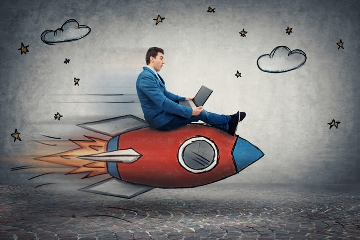 A businessman looking at his laptop while riding a cartoon rocket.