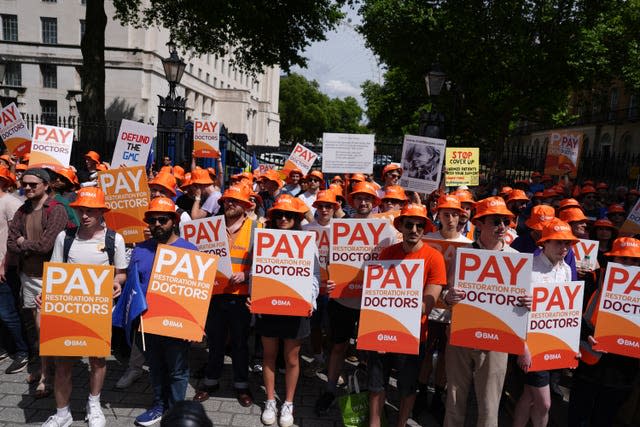 A large group of young doctors on strike, wearing orange BMA caps and holding banners reading 