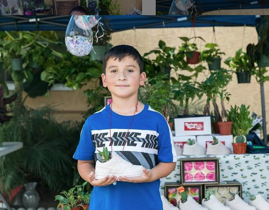 Eight-year-old Aaron poses in his garden holding a shoe with a succulent in it.