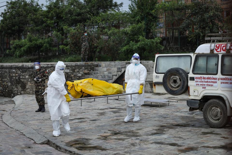 Workers in protective suits carry a body on a stretcher