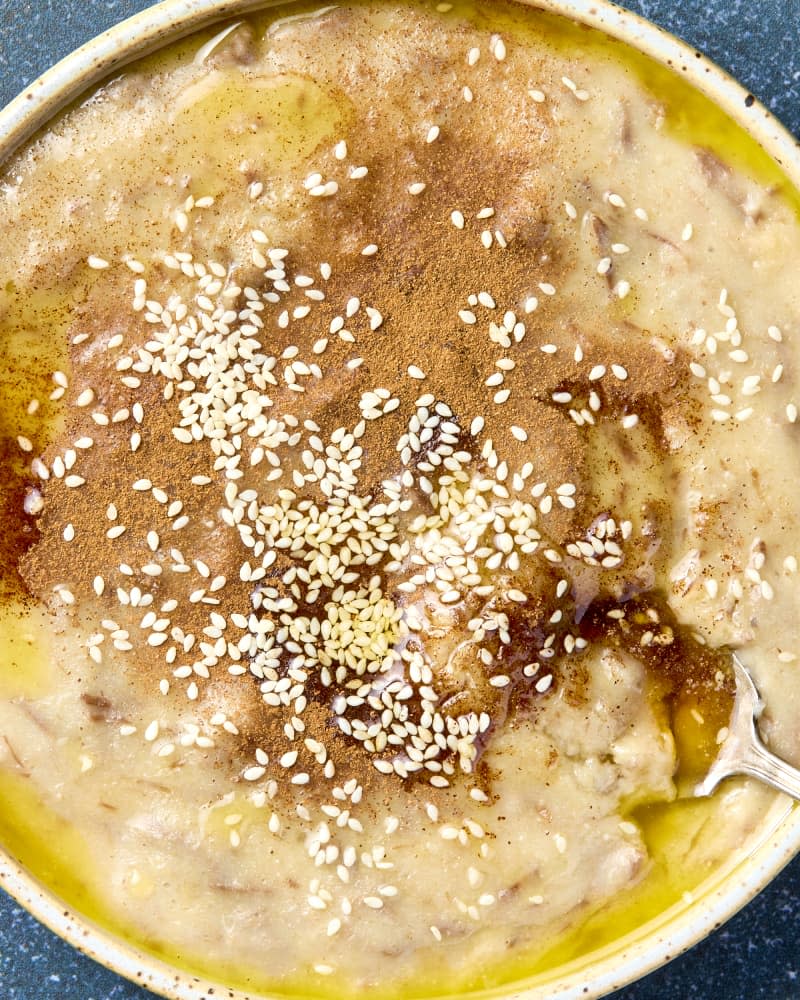 overhead shot of haleem in a white bowl, topped with cinnamon and sesame seeds.