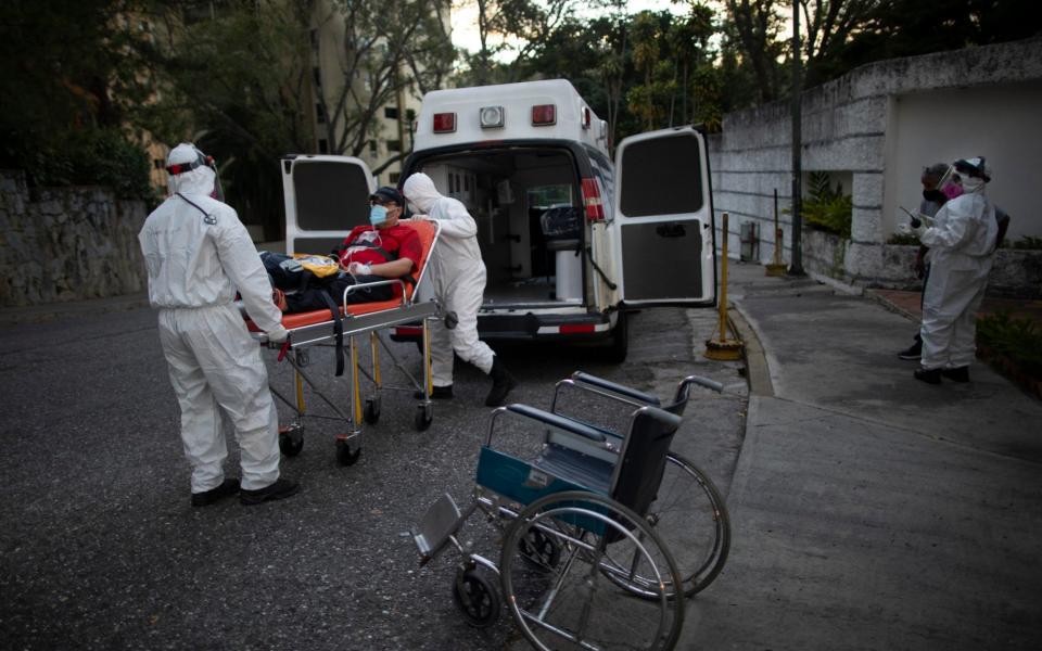 Angels on the Road volunteer paramedics move a person suspected of having Covid-19 to a hospital in Caracas, Venezuela - Ariana Cubillos/AP