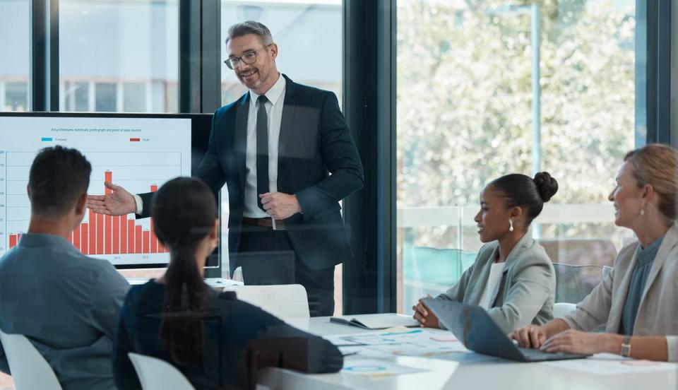 A sales team meets in an office and views customer data on a large screen.