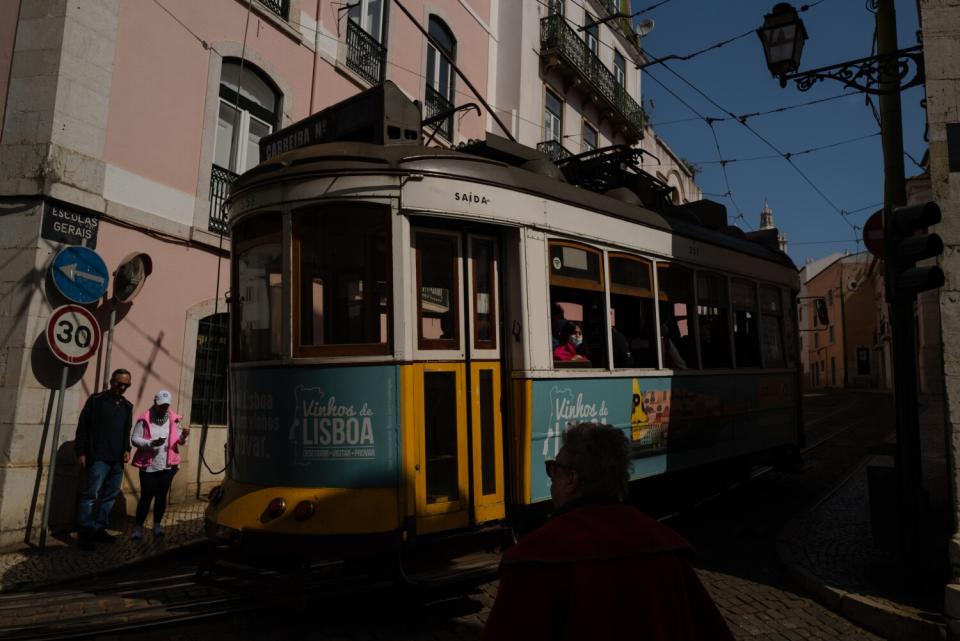 A blue, white and yellow tram next to a building and pedestrians