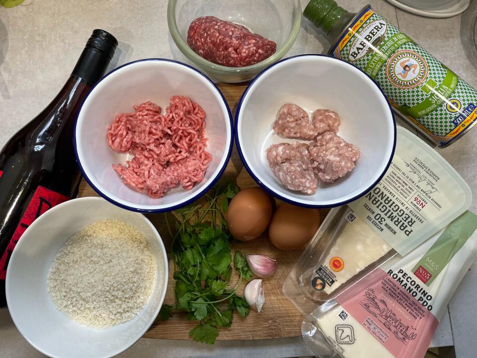 three types of meat, wine, cheese, flour and other ingredients for ina garten's meatballs on a wooden cutting board