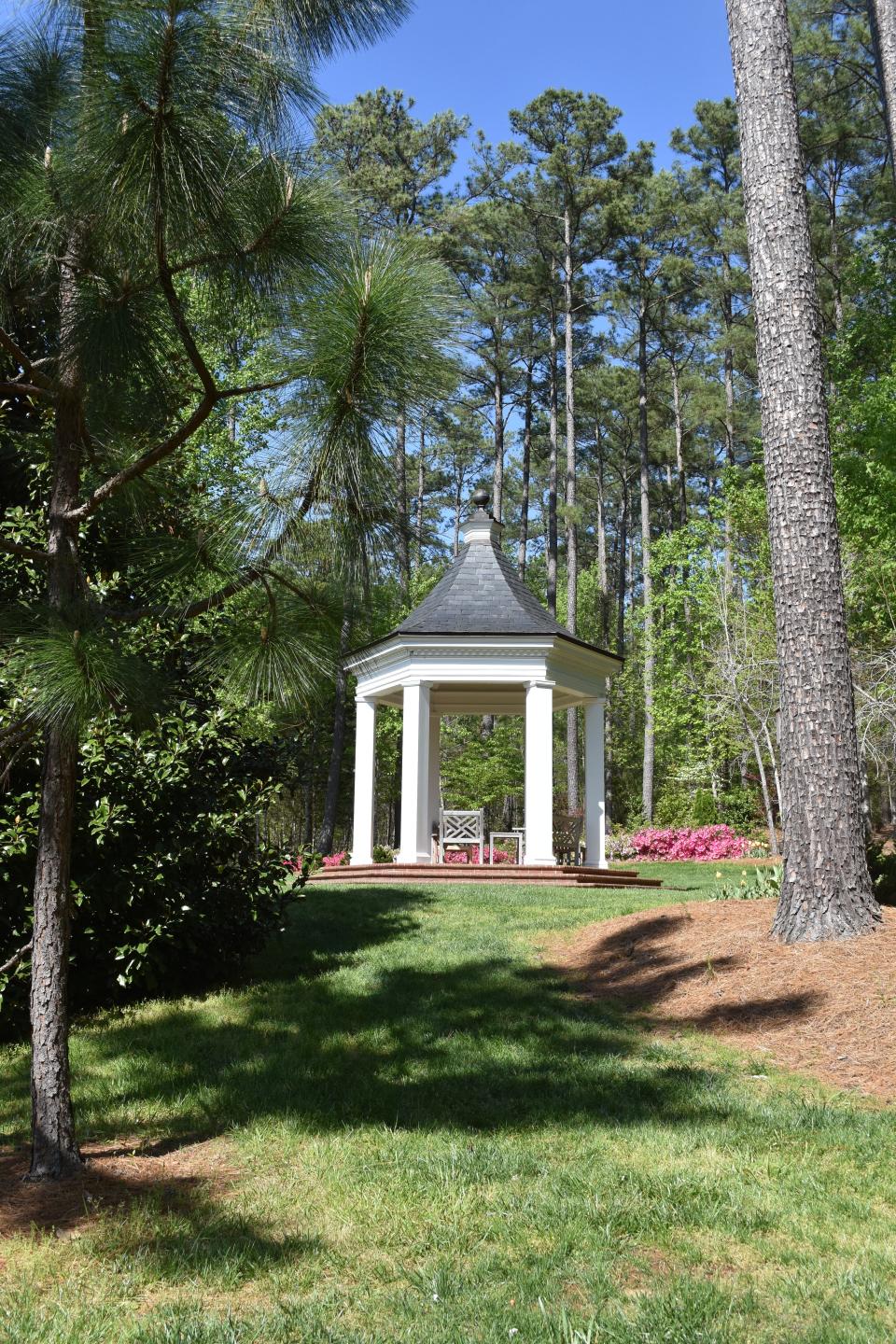A hexagonal gazebo provides a shady spot to sit and rest on the far side of the pond at Betty Montgomery's garden in Campobello SC. April 2022