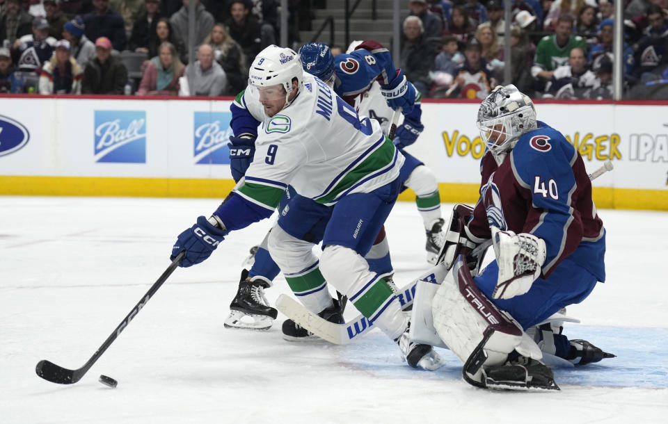 Vancouver Canucks center J.T. Miller, front left, reaches out for the puck next to Colorado Avalanche defenseman Cale Makar (8), while goaltender Alexandar Georgiev watches during the second period of an NHL hockey game Wednesday, Nov. 22, 2023, in Denver. (AP Photo/David Zalubowski)