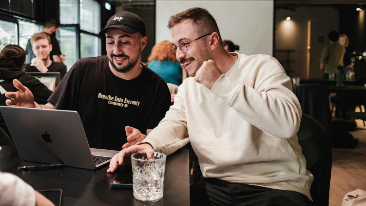  Two men using laptop in crowded cafe. 