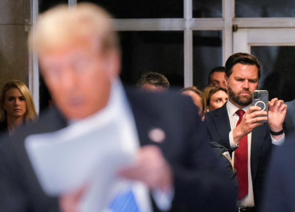 JD Vance takes pictures as Donald Trump speaks to reporters. via REUTERS