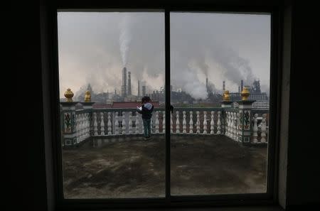 A girl reads a book on her balcony as smoke rises from chimneys of a steel plant, on a hazy day in Quzhou, Zhejiang province April 3, 2014. REUTERS/Stringer