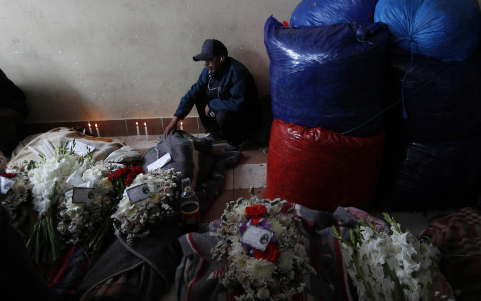 Bus crash victims lie on the ground surrounded by flowers and candles at the coca leaf market where the late farmers used to bring their coca harvest to sell in La Paz, Bolivia, Friday, Jan. 31, 2020. A bus missed a curve on a road near Bolivia’s capital on Friday and plunged down a ravine, killing at least 14 people and injuring 19 more, officials said. (AP Photo/Juan Karita)