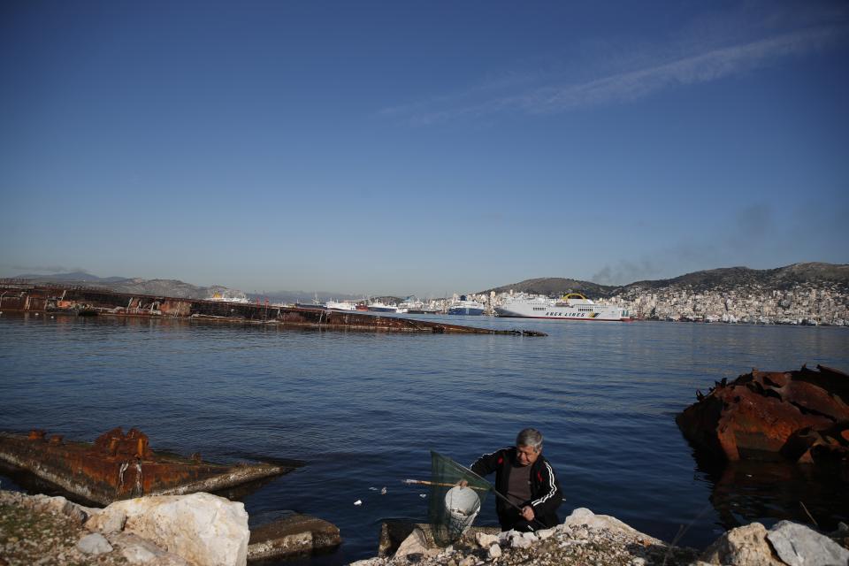 A man holds a bucket with fish in Damari, an area with eleven shipwrecks, on Salamina island, west of Athens, on Thursday, Jan. 31, 2020. Greece this year is commemorating one of the greatest naval battles in ancient history at Salamis, where the invading Persian navy suffered a heavy defeat 2,500 years ago. But before the celebrations can start in earnest, authorities and private donors are leaning into a massive decluttering operation. They are clearing the coastline of dozens of sunken and partially sunken cargo ships, sailboats and other abandoned vessels. (AP Photo/Thanassis Stavrakis)