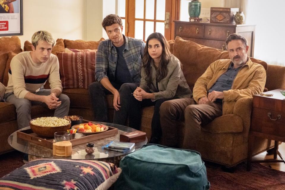 Dylan's character sitting with David Arquette and others in a living room in a scene from Scream