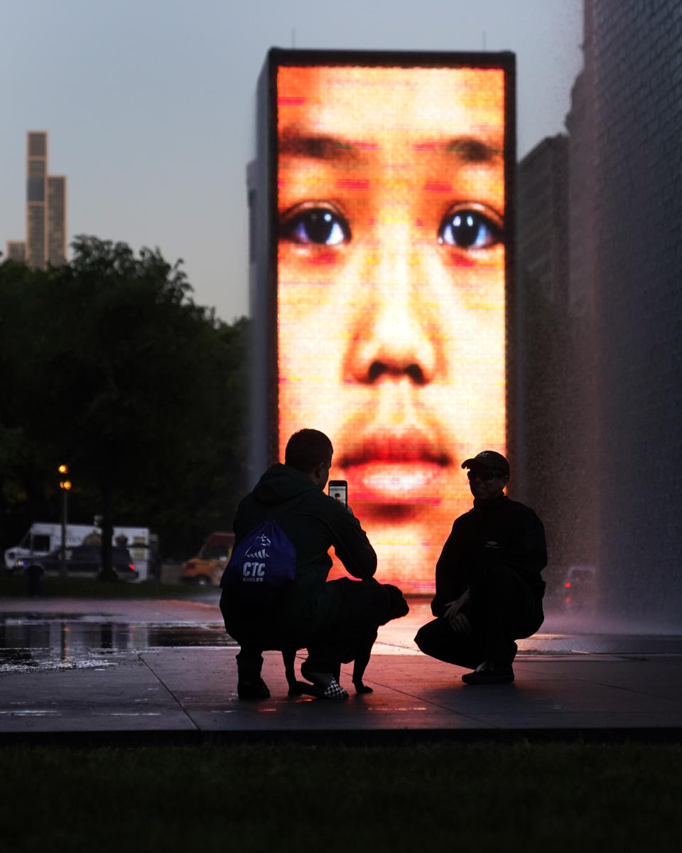 Two visitors at the Crown Fountain in Chicago's Millennium Park make a photograph Thursday, May 25, 2023. Chicago is heading into the Memorial Day weekend hoping to head off violence that tends to surge with rising temperatures of summer. Even the state of Illinois is assisting by sending in what it's called "peacekeepers" in an attempt to deescalate violent situations. (AP Photo/Charles Rex Arbogast)