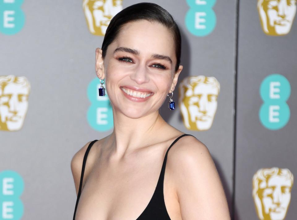 Emilia wears a simple black sleeveless dress on a red carpet