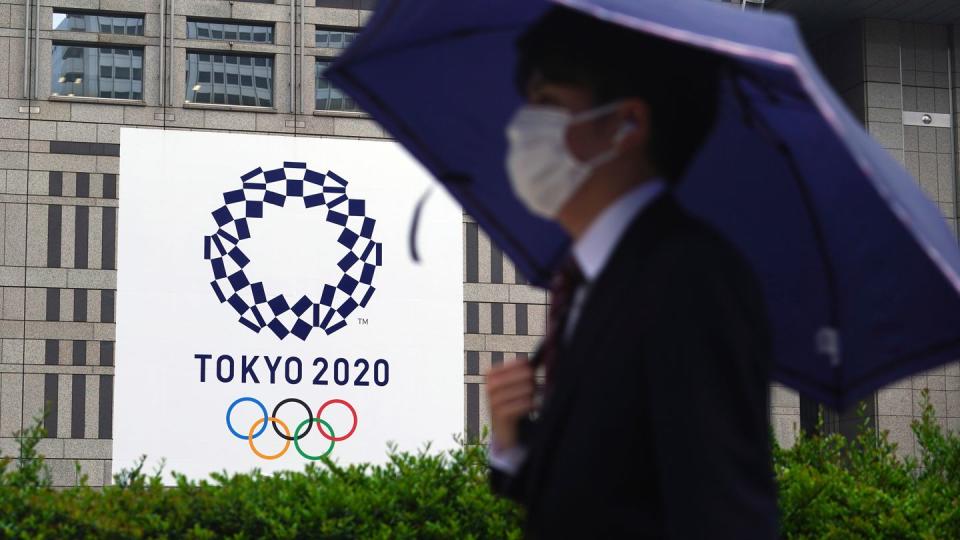 Ein Mann mit Mund-Nasen-Schutz geht im Regen an einem Banner der Olympischen Spiele Tokio 2020 vorbei.