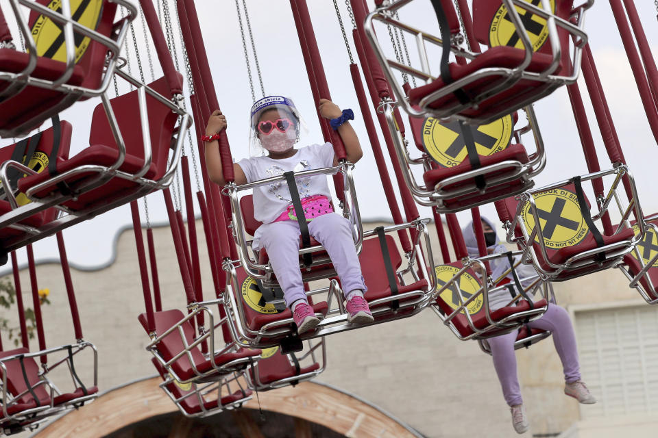 A young girl wearing a protective face shield enjoys a swing ride as physical distancing markings are seen on the seats during the first day of the reopening of Dunia Fantasi Amusement Park after weeks of closure due to the large-scale restrictions imposed to help curb the new coronavirus outbreak, at Ancol Dream Park in Jakarta, Indonesia, Saturday, June 20, 2020. (AP Photo/Tatan Syuflana)