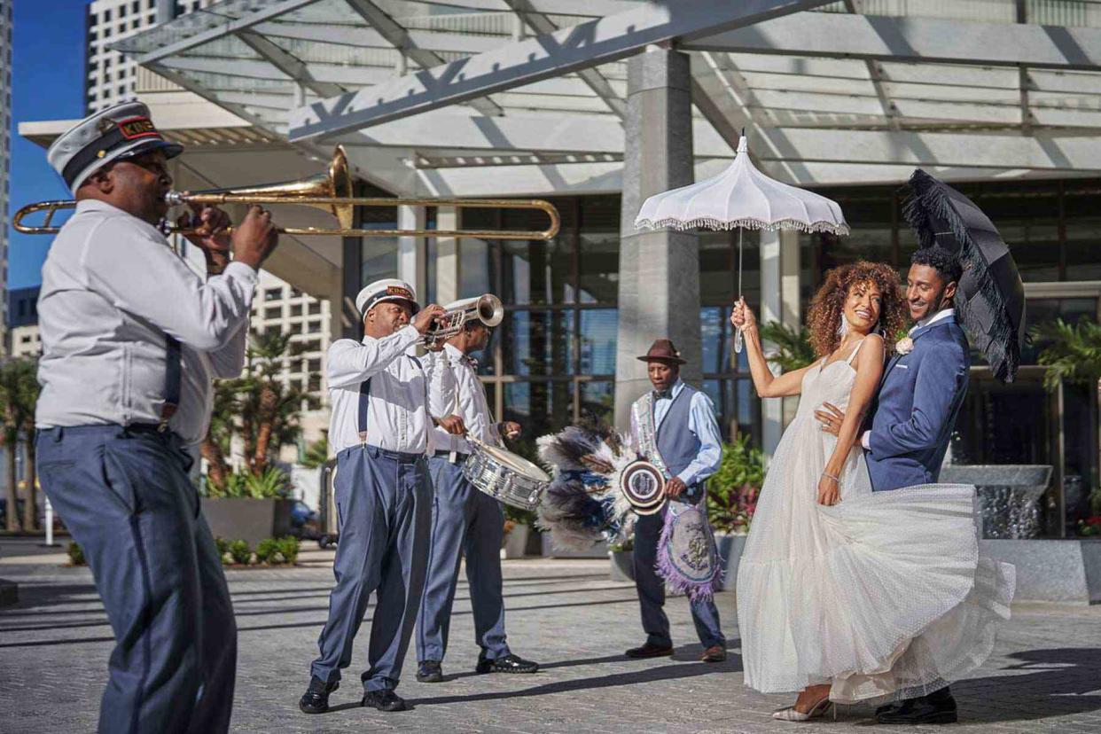 <p>Christian Horan/Courtesy of Four Seasons Hotels and Resorts</p> A bride and groom walk with a jazz band at the Four Seasons Hotel New Orleans.