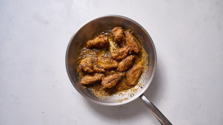 chicken wings tossed in sauce in pan