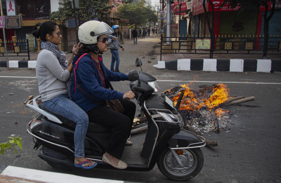 Commuters ride past fire set by protestors in Gauhati, India, Thursday, Dec. 12, 2019. Police arrested dozens of people and enforced curfew on Thursday in several districts in India’s northeastern Assam state where thousands protested legislation granting citizenship to non-Muslims who migrated from neighboring countries. (AP Photo/Anupam Nath)