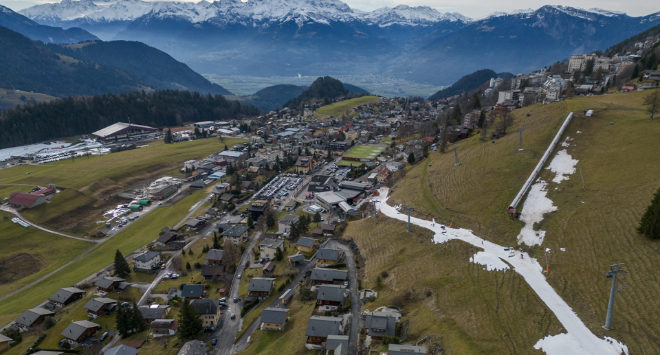 A tiny vein of man-made snow trickles down a hillside at Leysin, Austria. Mountains in the background.