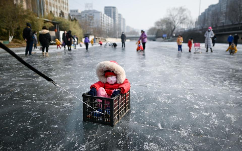 A man pulls a child sitting in a box on a frozen river in Beijing - WANG ZHAO/AFP