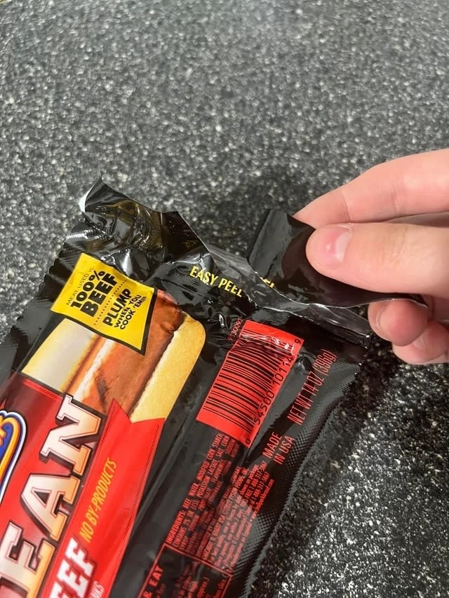 Someone tearing off a piece of a package of hot dogs labeled 'Easy peel'