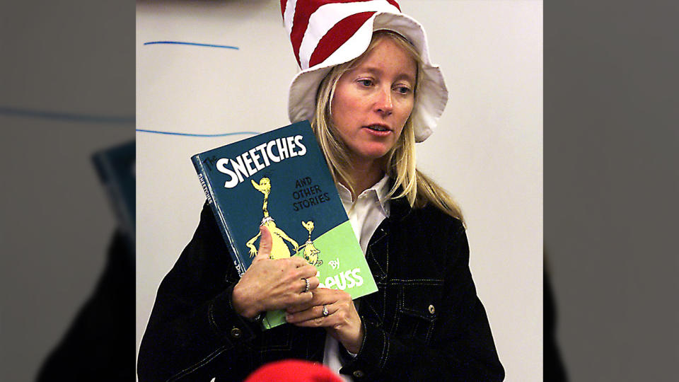 Jill Doran, holding a copy of the book, wears a tall hat with red-and-white stripes referring to Dr. Suess's book The Cat in the Hat. 