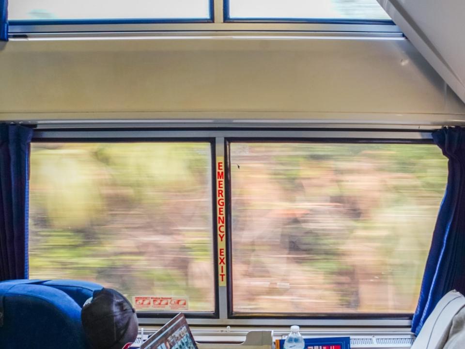 Inside an Amtrak bedroom with blue seats and a big window showing nature outside